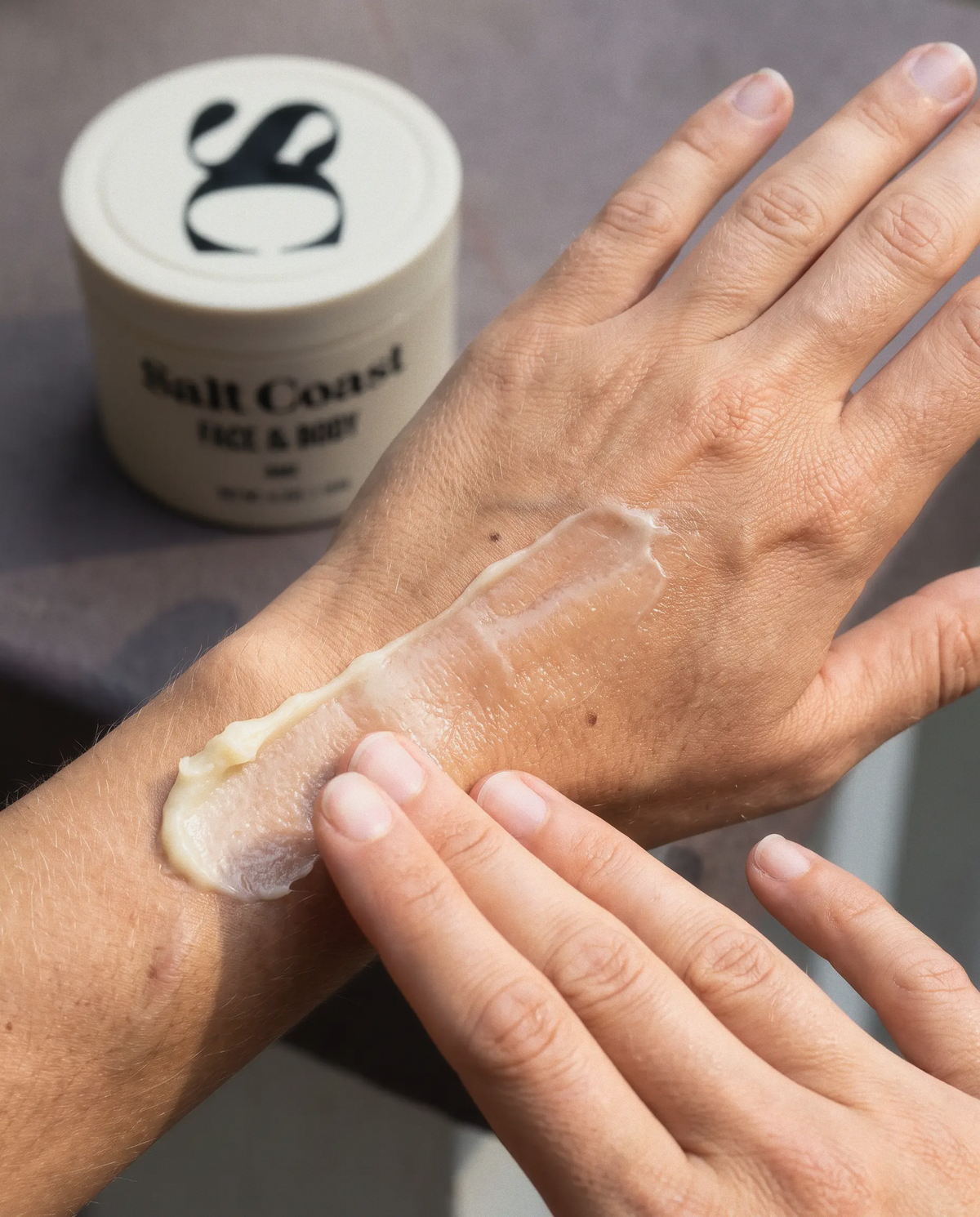 Applying Salt Coast Bare tallow balm to the back of a hand, jar in the background