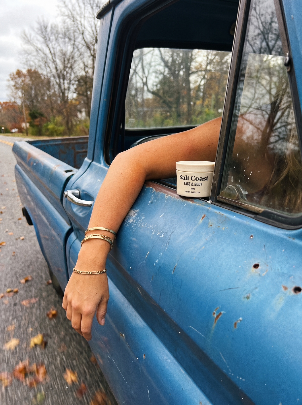 Arm resting out of a blue truck window holding a jar of Salt Coast Bare tallow balm