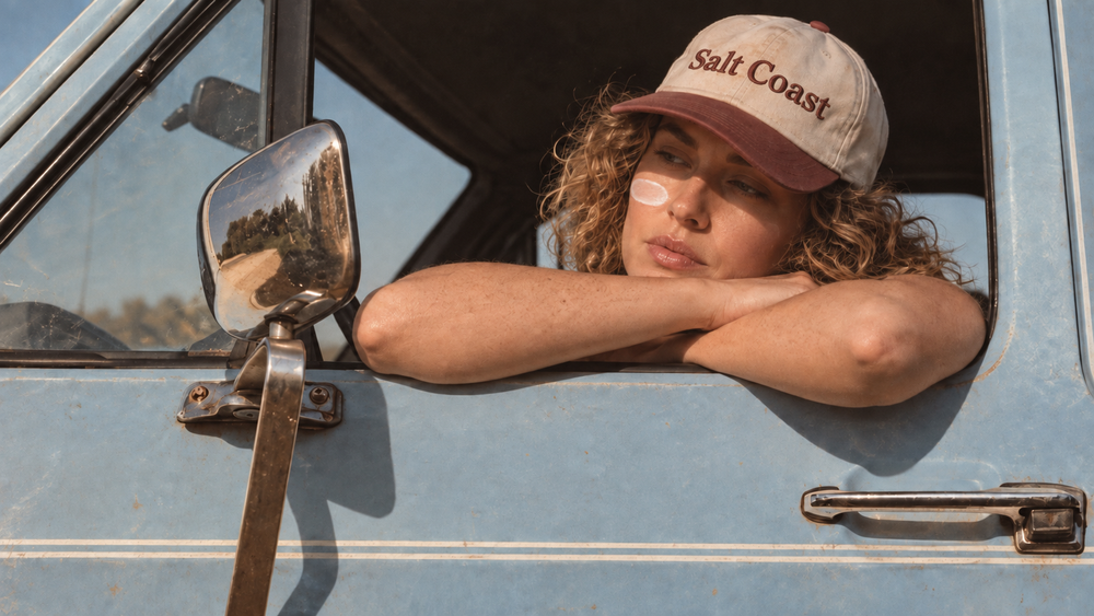 Woman in a Salt Coast cap leaning out of a vintage truck window